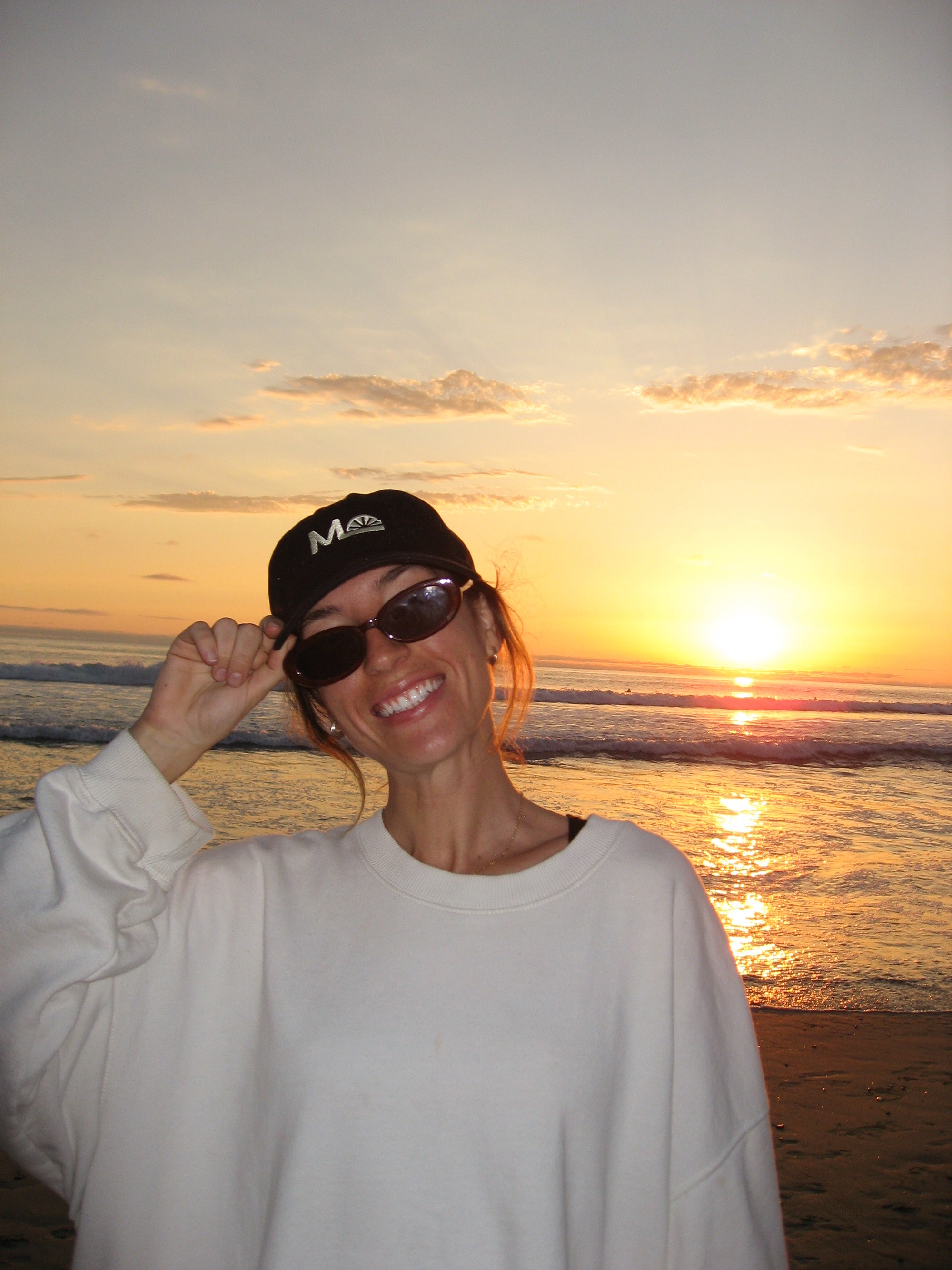 Person wearing sunglasses and a  Morning Light branded cap at sunset on a beach