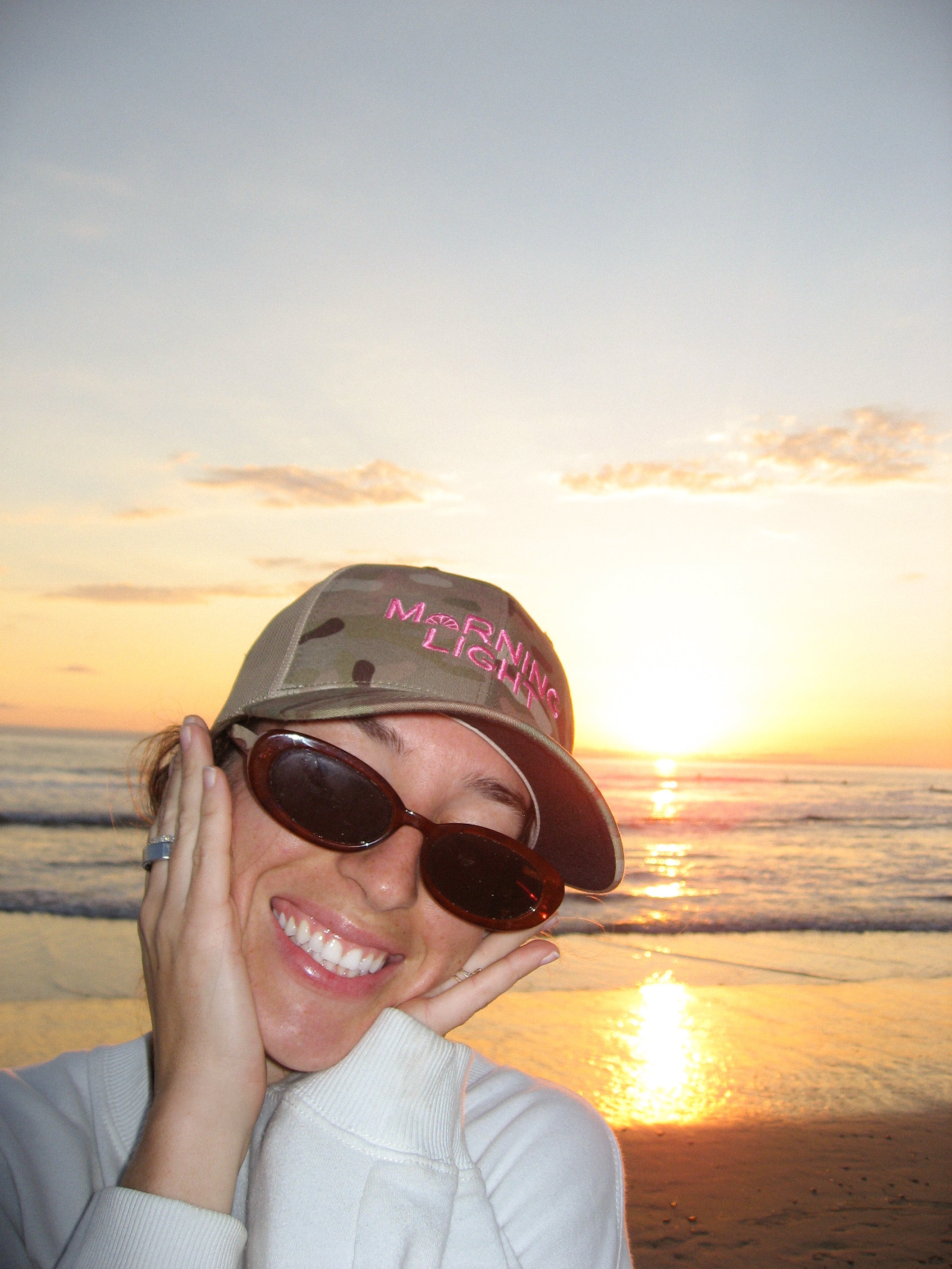 Person wearing a cap and sunglasses with a sunset over water in the background