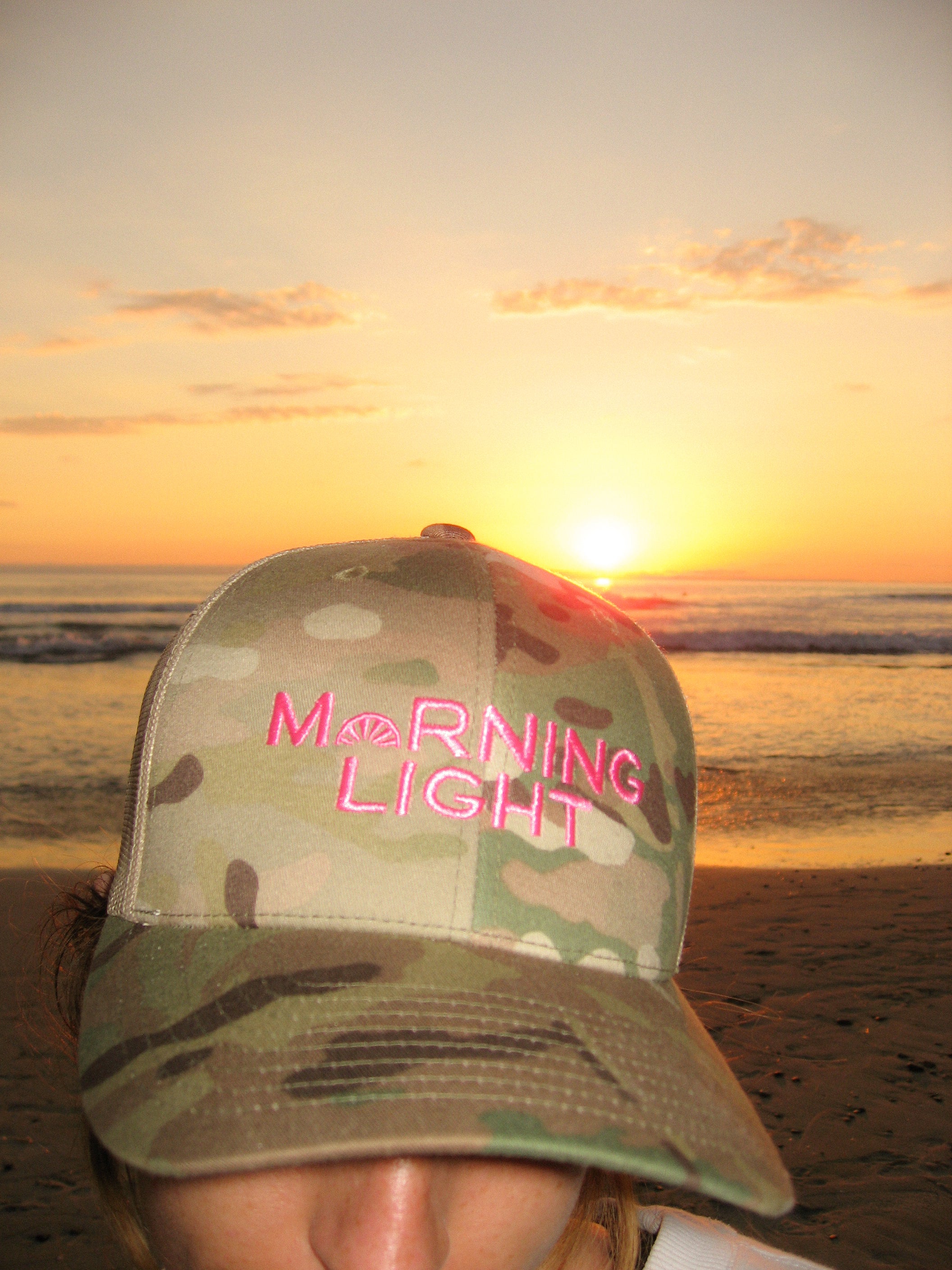 Camouflage cap with 'Morning Light' text at sunset on a beach