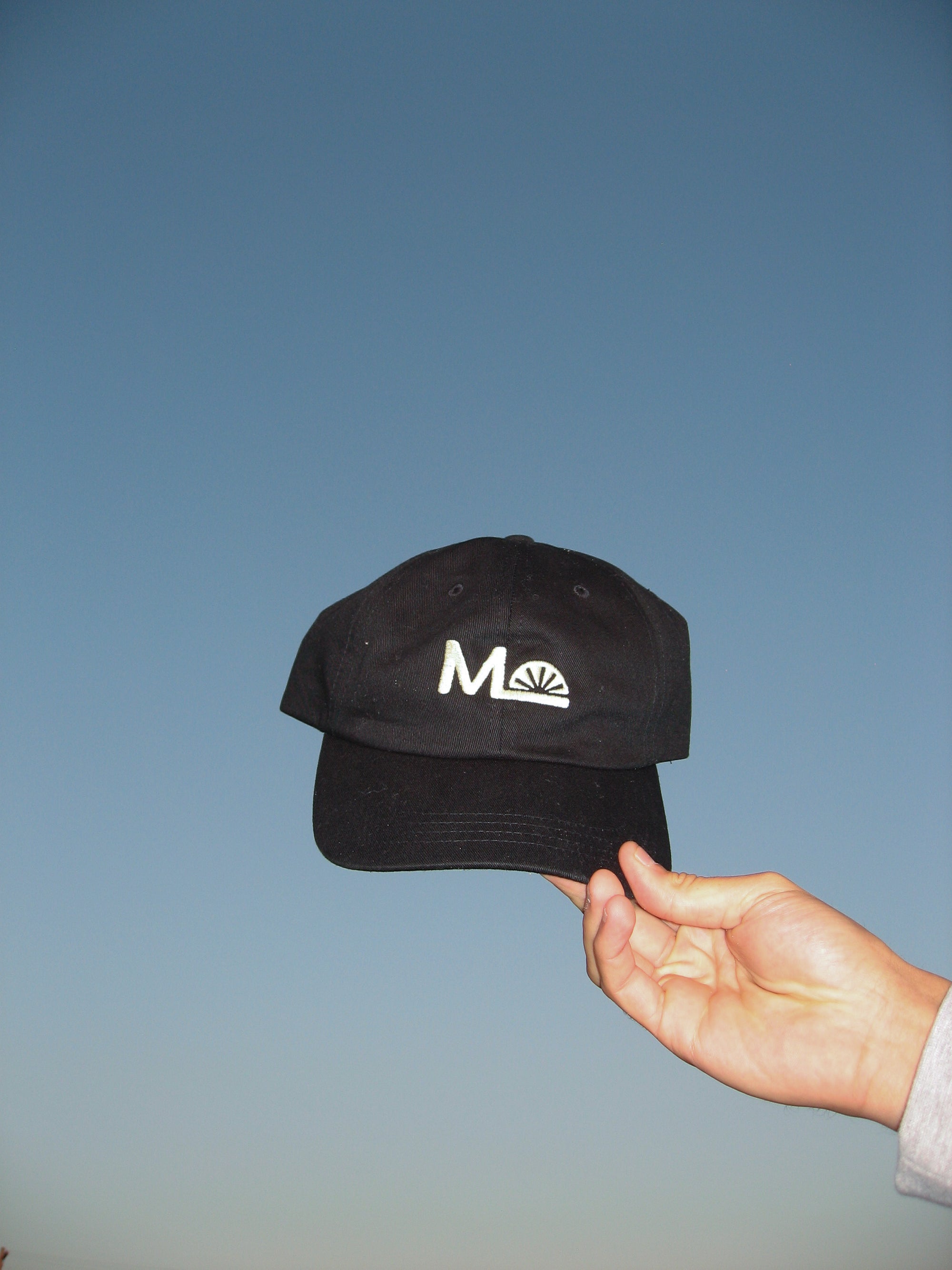 Black cap with a logo held by a hand against a blue sky